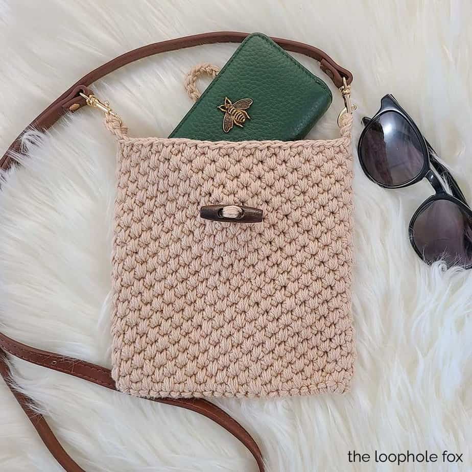 Beige crocheted bag on fur carpte with wallet and sunglasses.