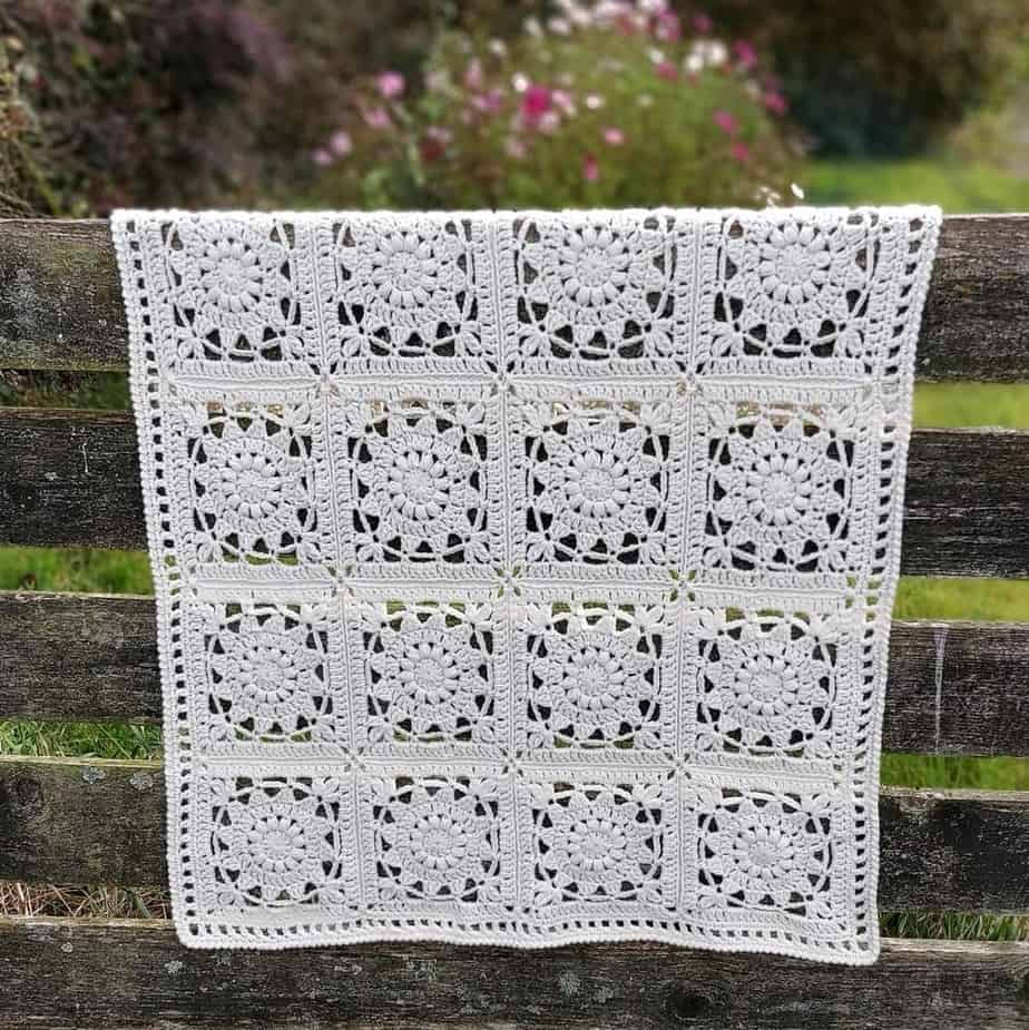 White crochet blanket hanging over fence.