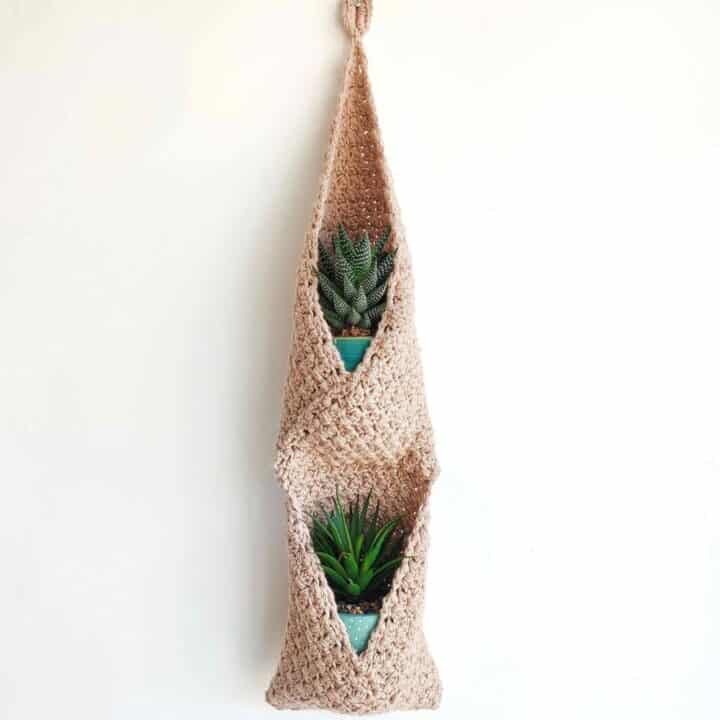 Crocheted hanging basket with two plants in it.