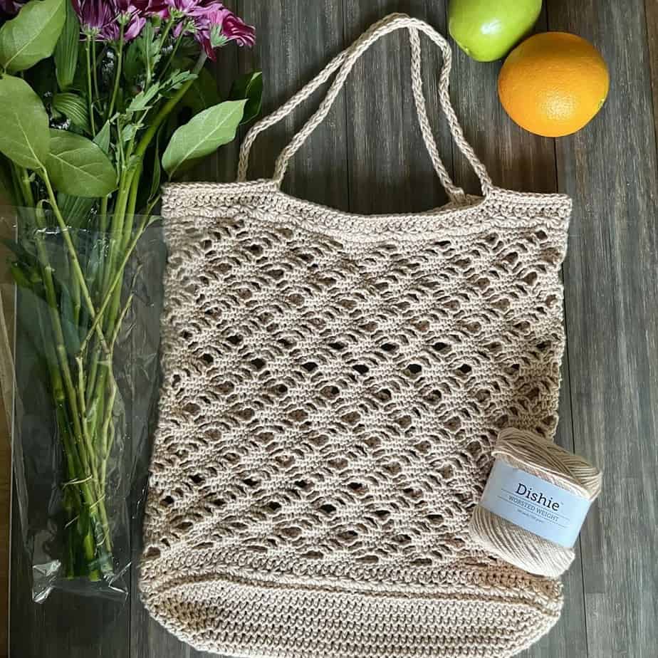 Beige crochet tote bag on a table with oranges and flowers.