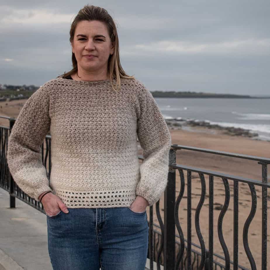 Woman wearing sweater, standing by the beach.