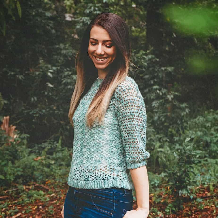 Woman standing outside wearing light green crochet top.