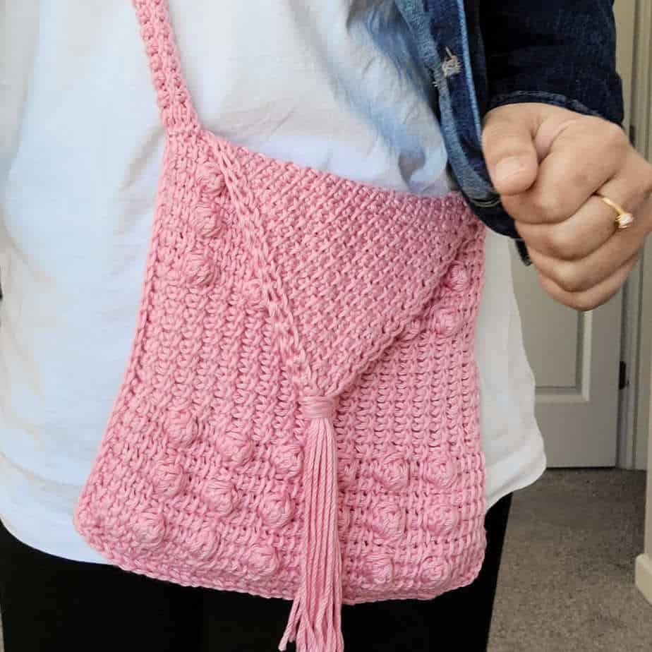 Close up of woman wearing pink crochet bag around her body.