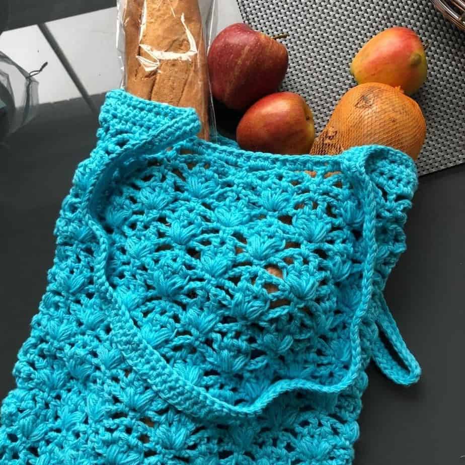 Blue crochet market bag with bread and fruit in it.