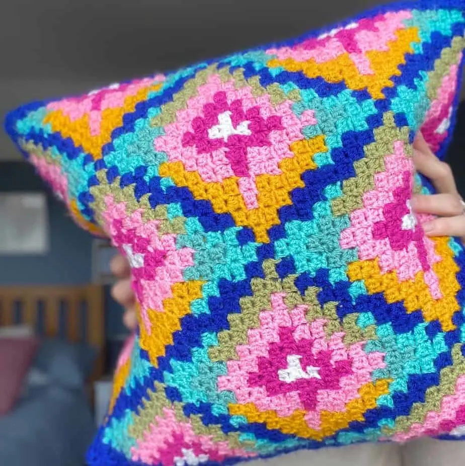 hands holding up colourful crochet cushion to the camera