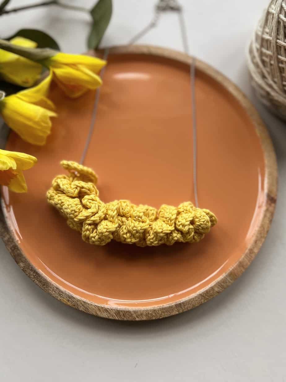 yellow crochet necklace pattern laying on orange dish with daffodils