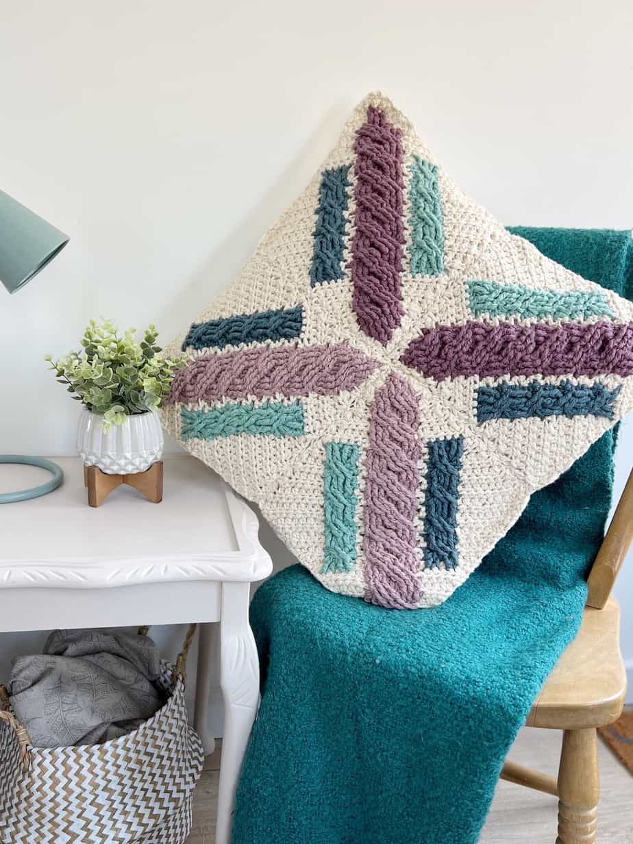 colour work cable crochet pillow pattern on wooden chair next to table