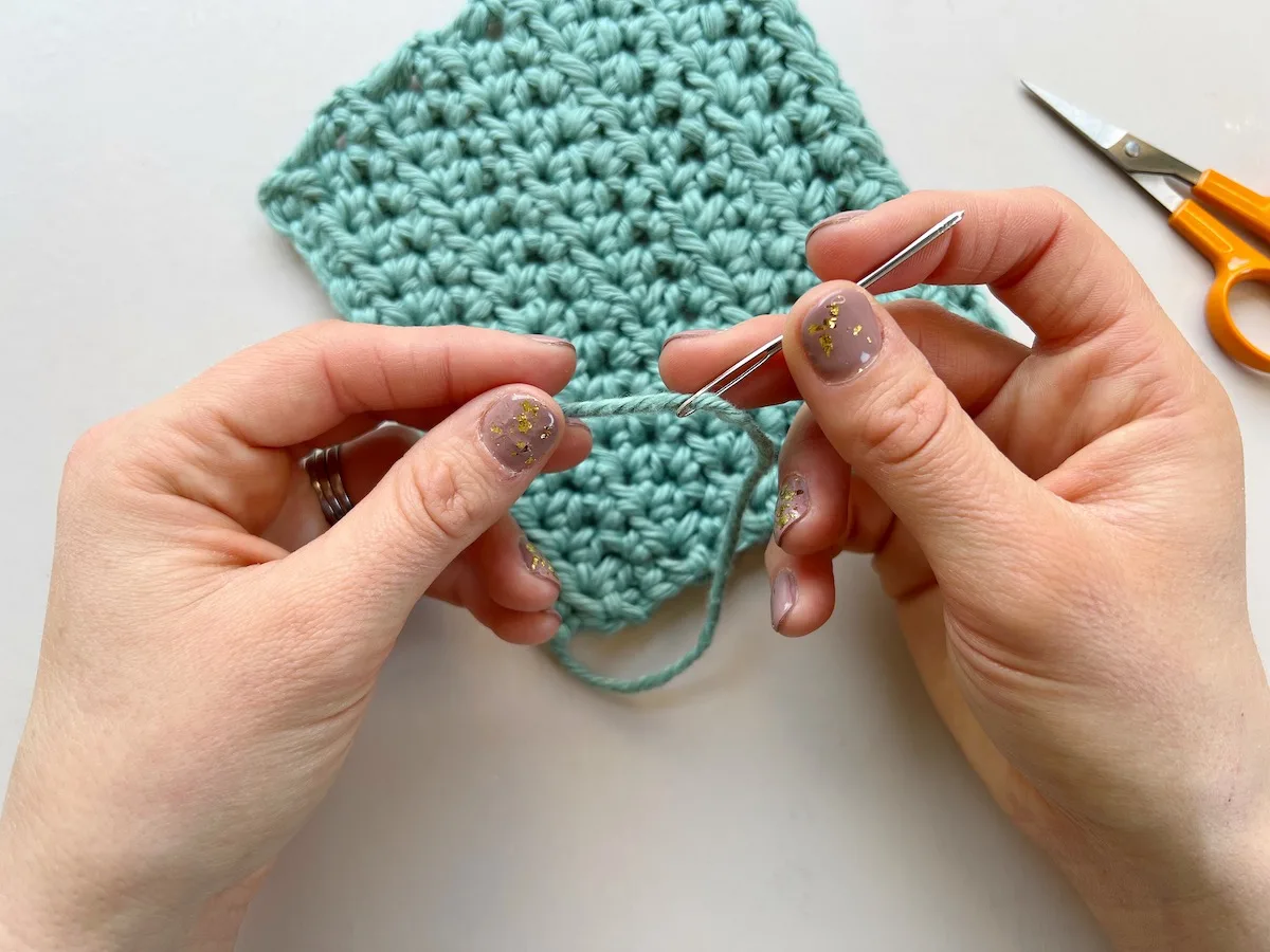 person threading a needle with blue yarn