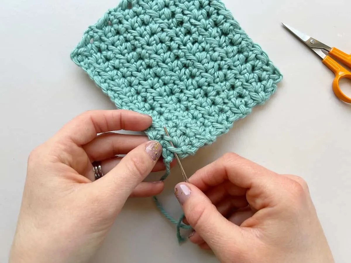 person showing how to weave in tails in crochet inserting needle through stitches