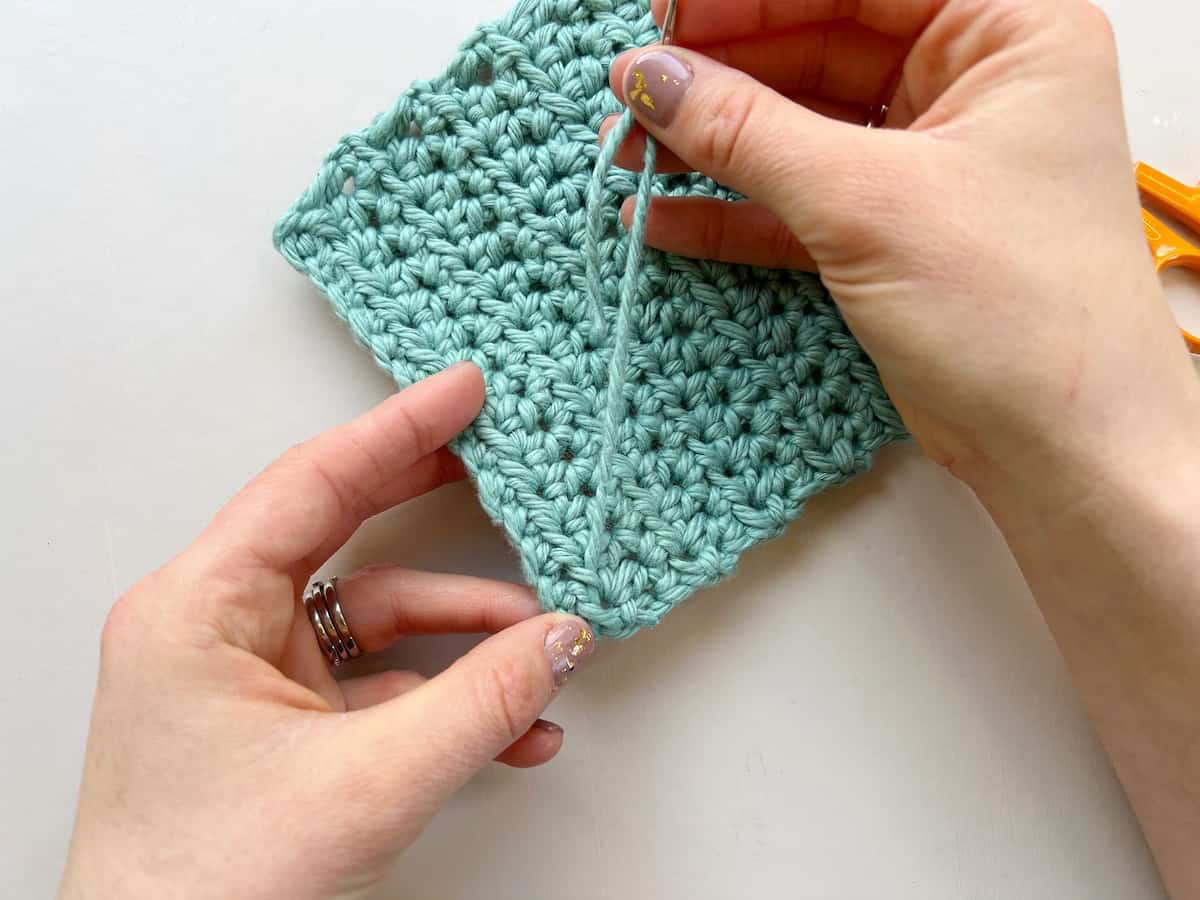 person sewing in ends in crochet pulling on yarn