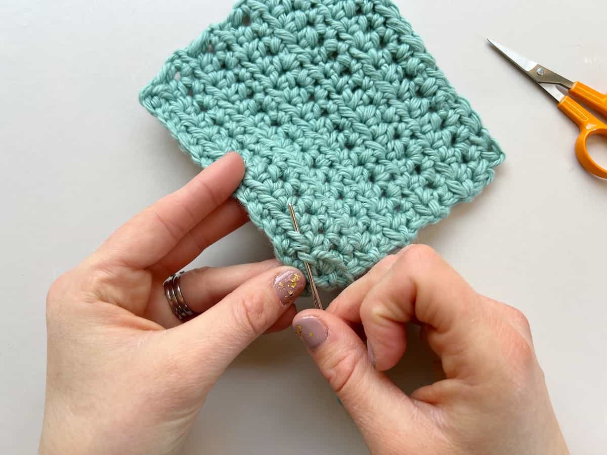 person weaving in tail of yarn in crochet