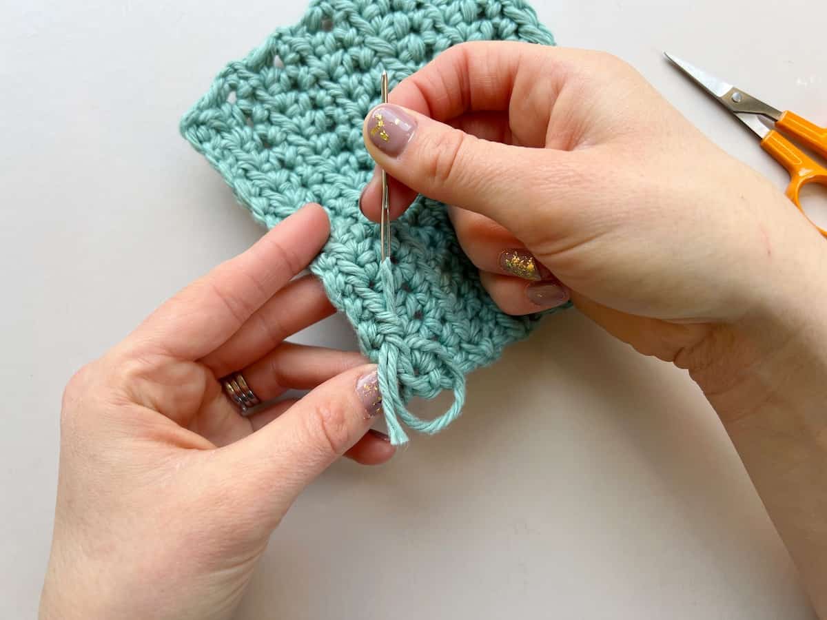 person showing how to weave in ends in crochet using needle and blue yarn