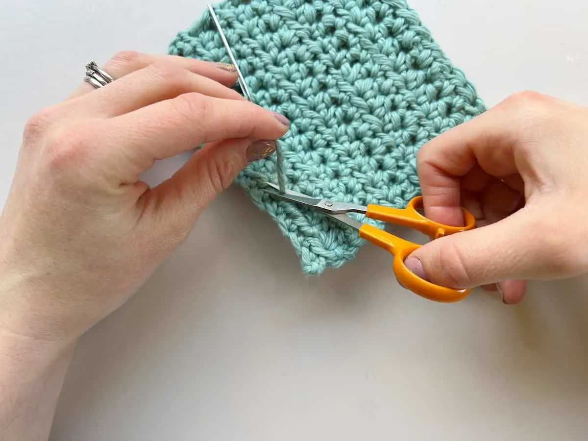 person cutting yarn with scissors after weaving in end of yarn