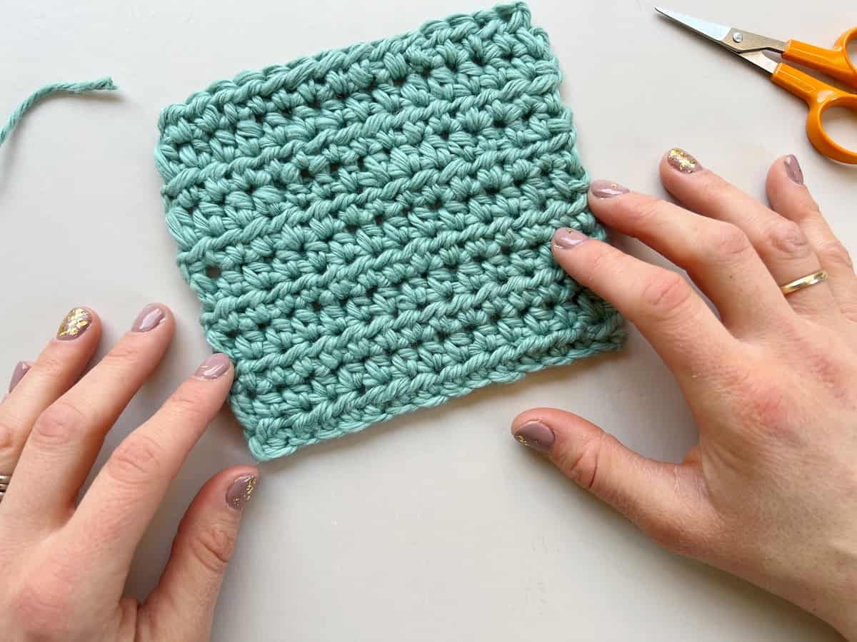 persons hands either side of small crochet square of half double crochet stitches and scissors in the background