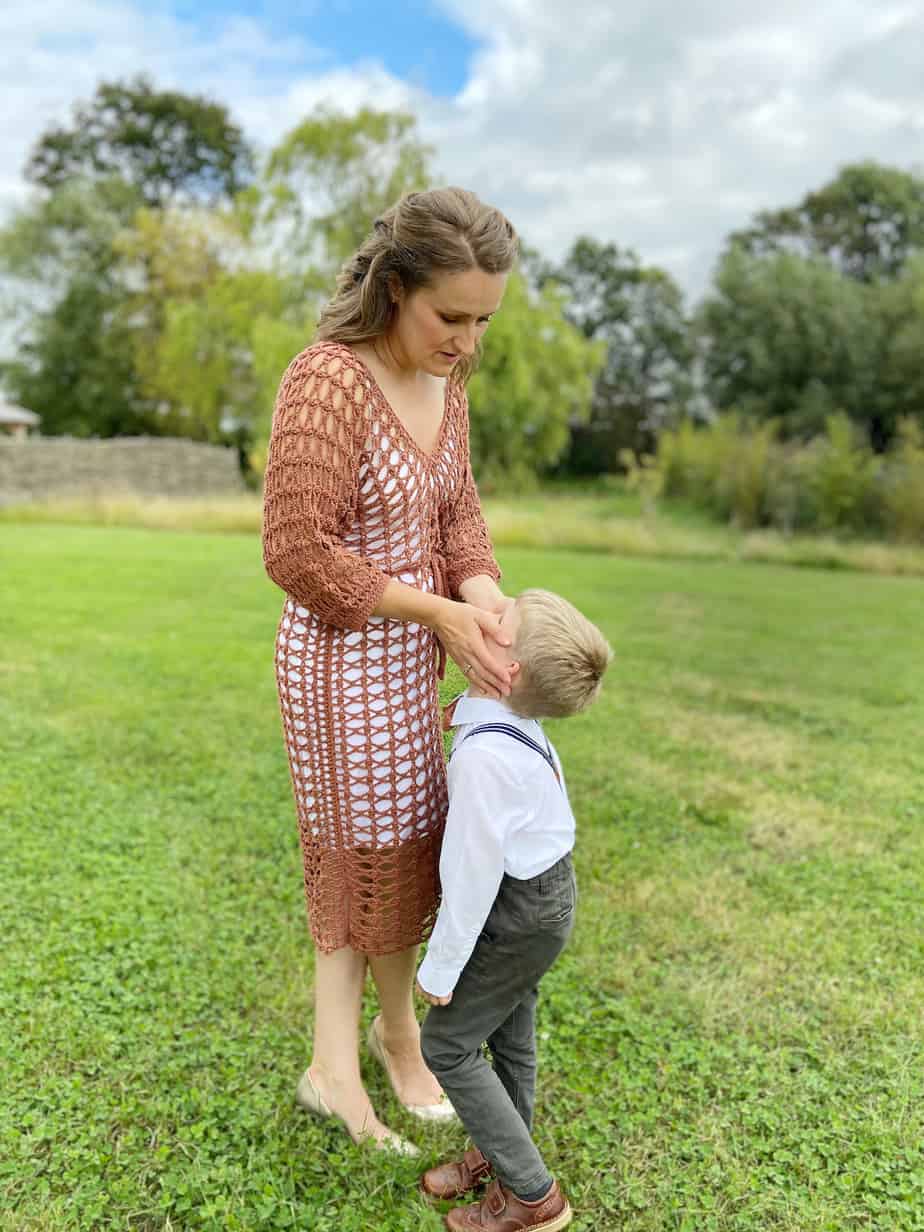 woman wearing crochet lace dress talking to child with her hands on his face