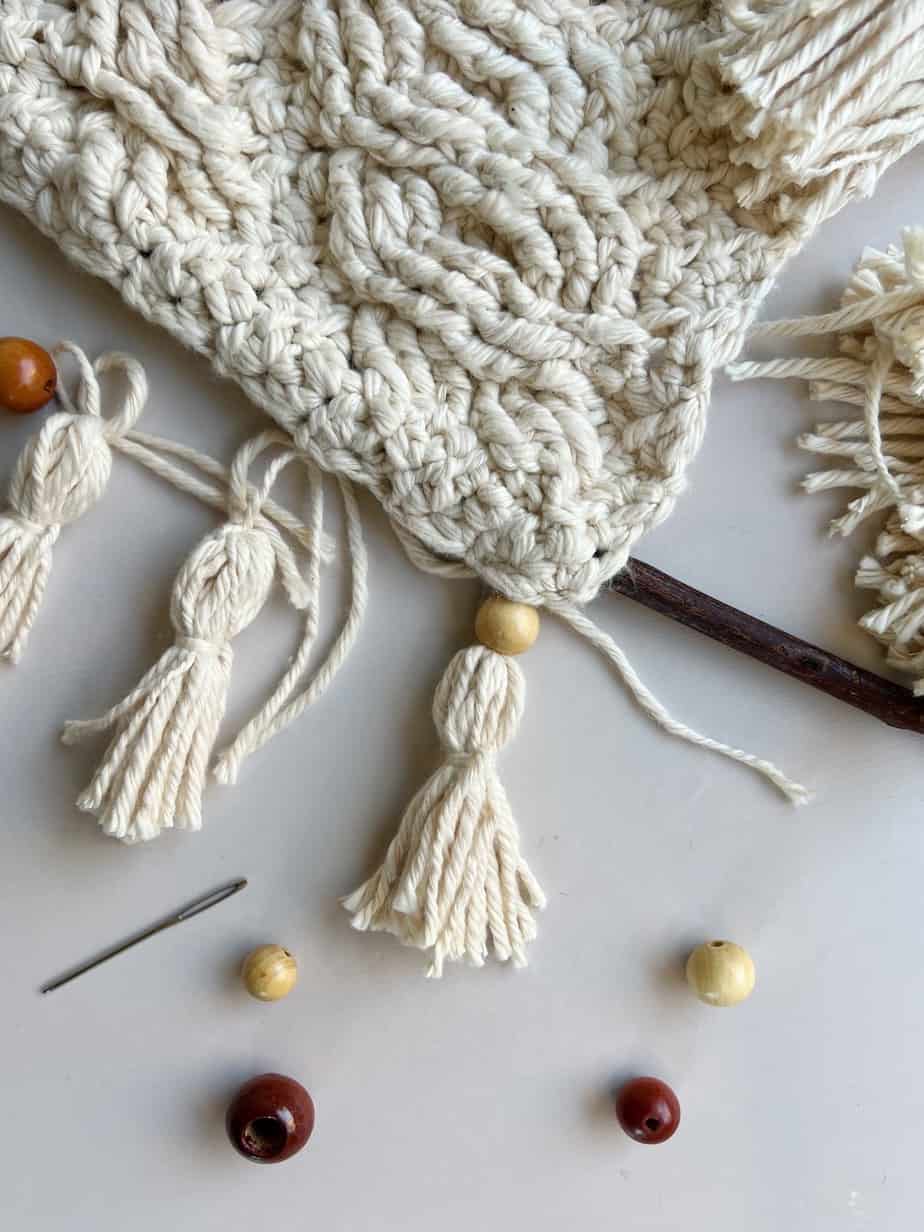 chunky tassels and beads being attached to crochet wall hanging