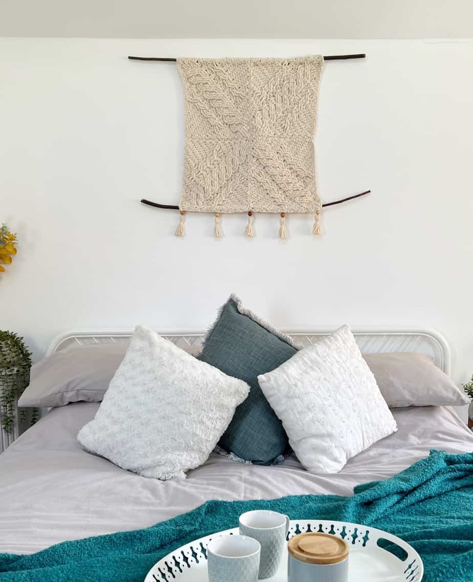 modern crochet wall hanging over bed with pillows, blankets and tray of tea
