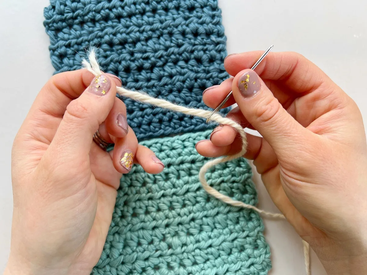 image showing person threading a needle in front of crochet squares