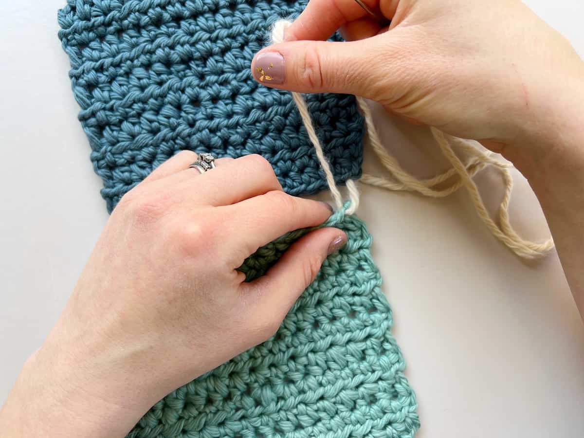 person carefully pulling yarn through a crochet square to join it with a whip stitch seam