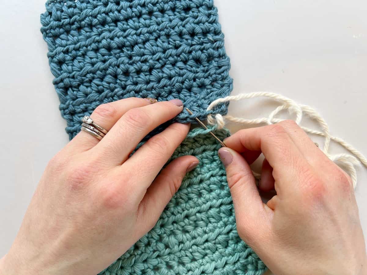 person inserting needle into 2 layers of crochet to create a whip stitch