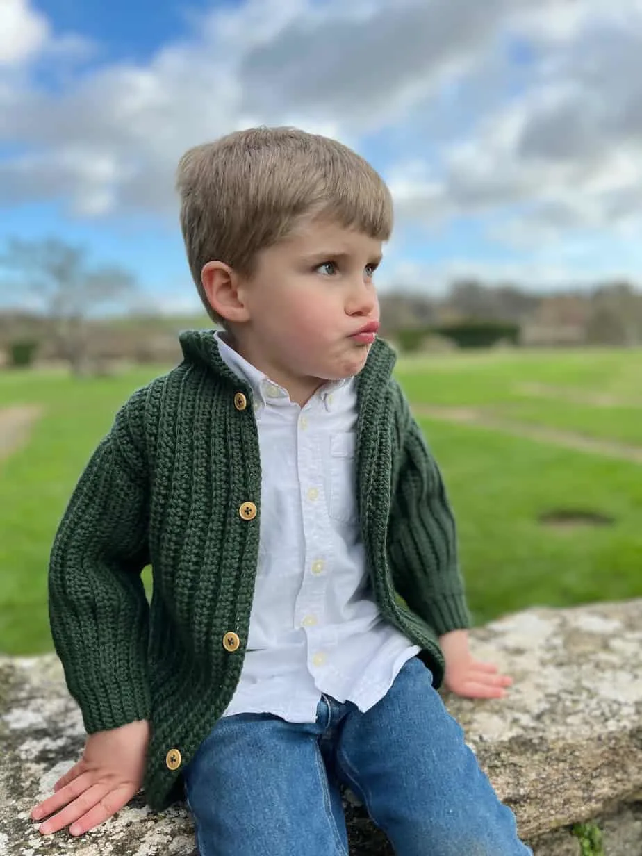 young boy wearing green crochet cardigan with wooden buttons and stand up collar