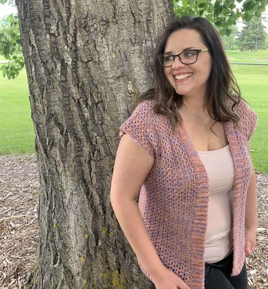 Short sleeve crochet cardigan pattern worn by woman leaning against a tree.