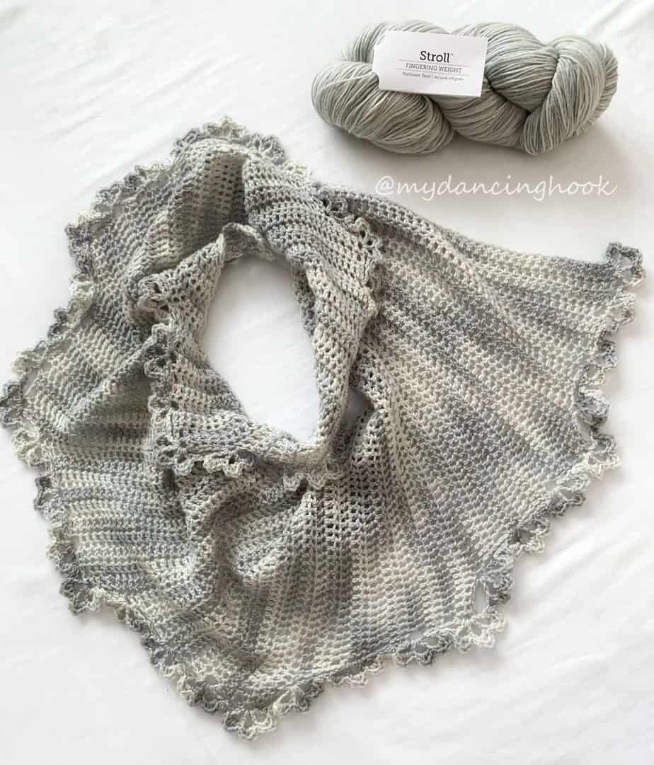 Delicate crochet shawlette laid flat with a hank of yarn beside it.