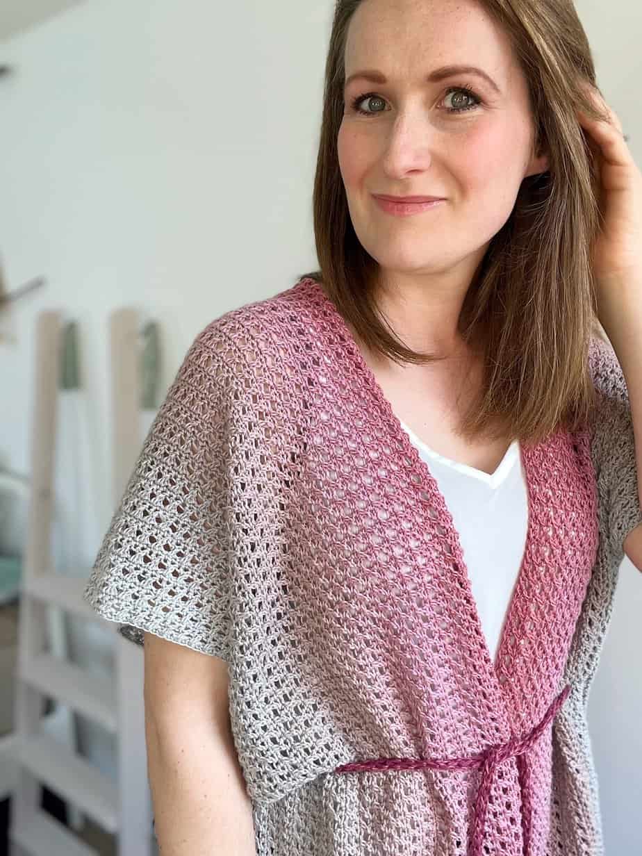 Woman smiling at camera wearing lacy crochet cardigan with a tie at the waist.