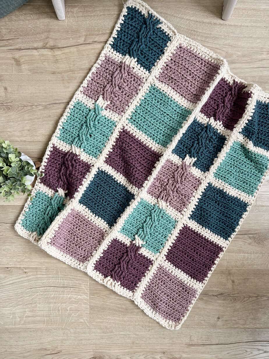Free patchwork crochet blanket pattern laid on wooden floor.