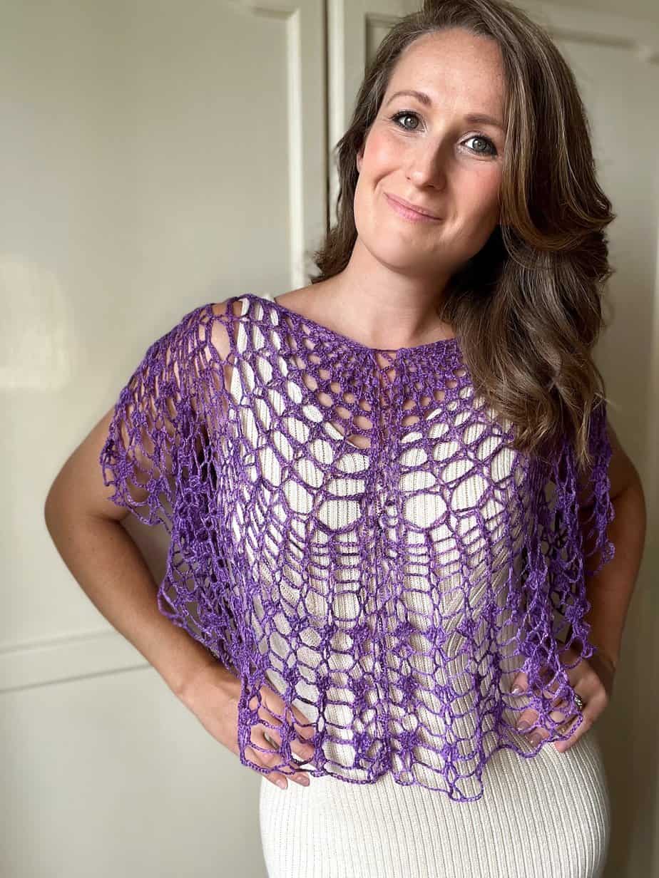 Woman with hands on hips in cream dress and purple crochet lace top pattern.
