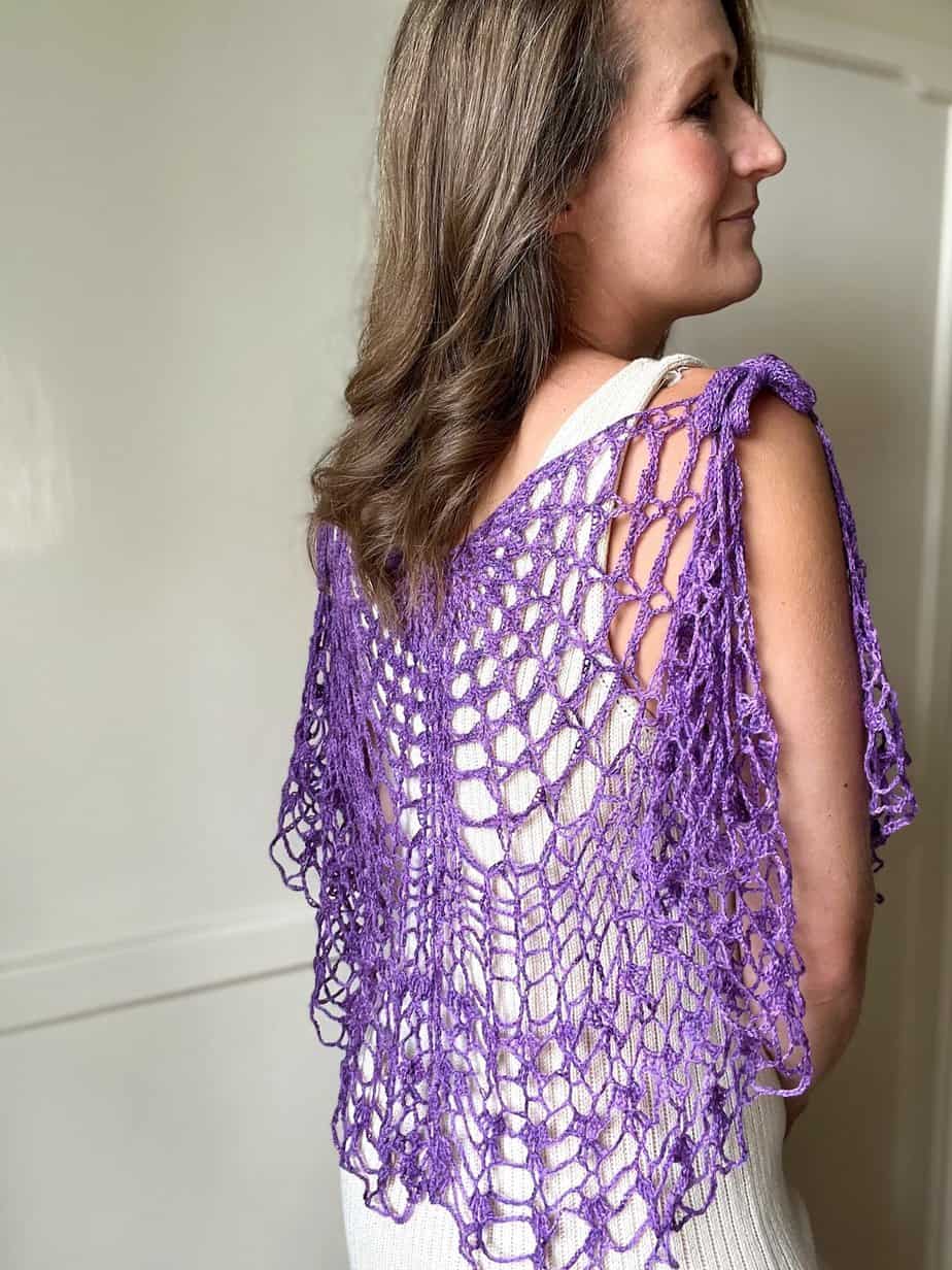 Woman facing away wearing lace crochet cape pattern with ties at shoulder.