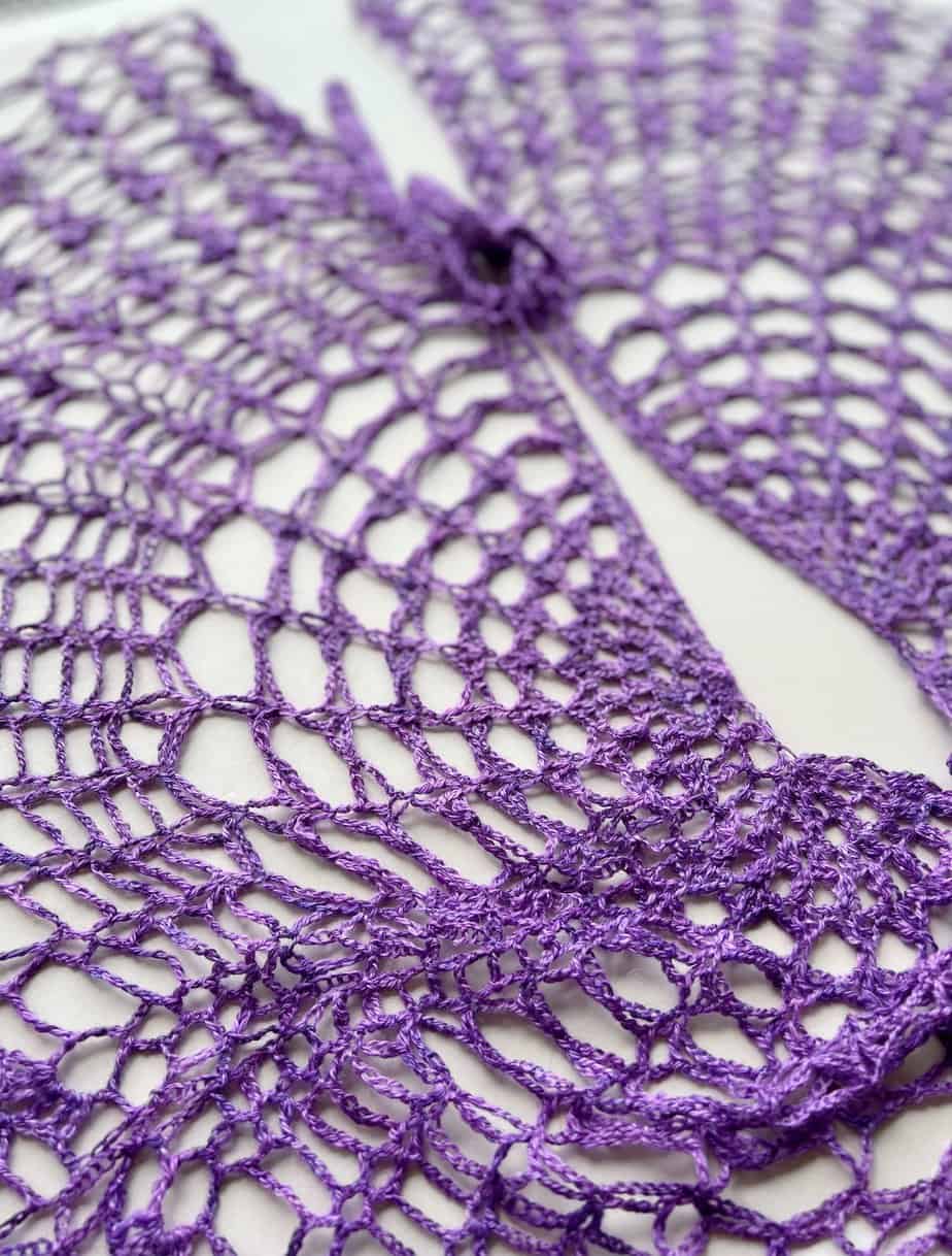 Purple crochet lace shawl pattern with tie laid flat on a table.