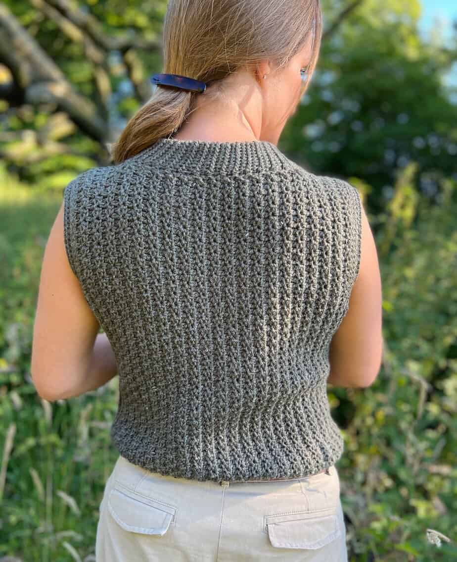Woman wearing sleeveless crochet top pattern with textured stitches facing away from camera.