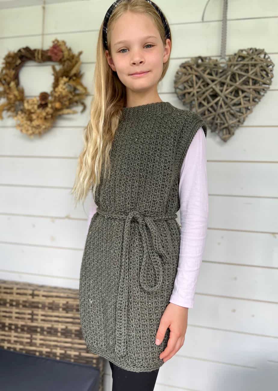 Child with long hair wearing a sleeveless crochet top tunic with tie around the waist.