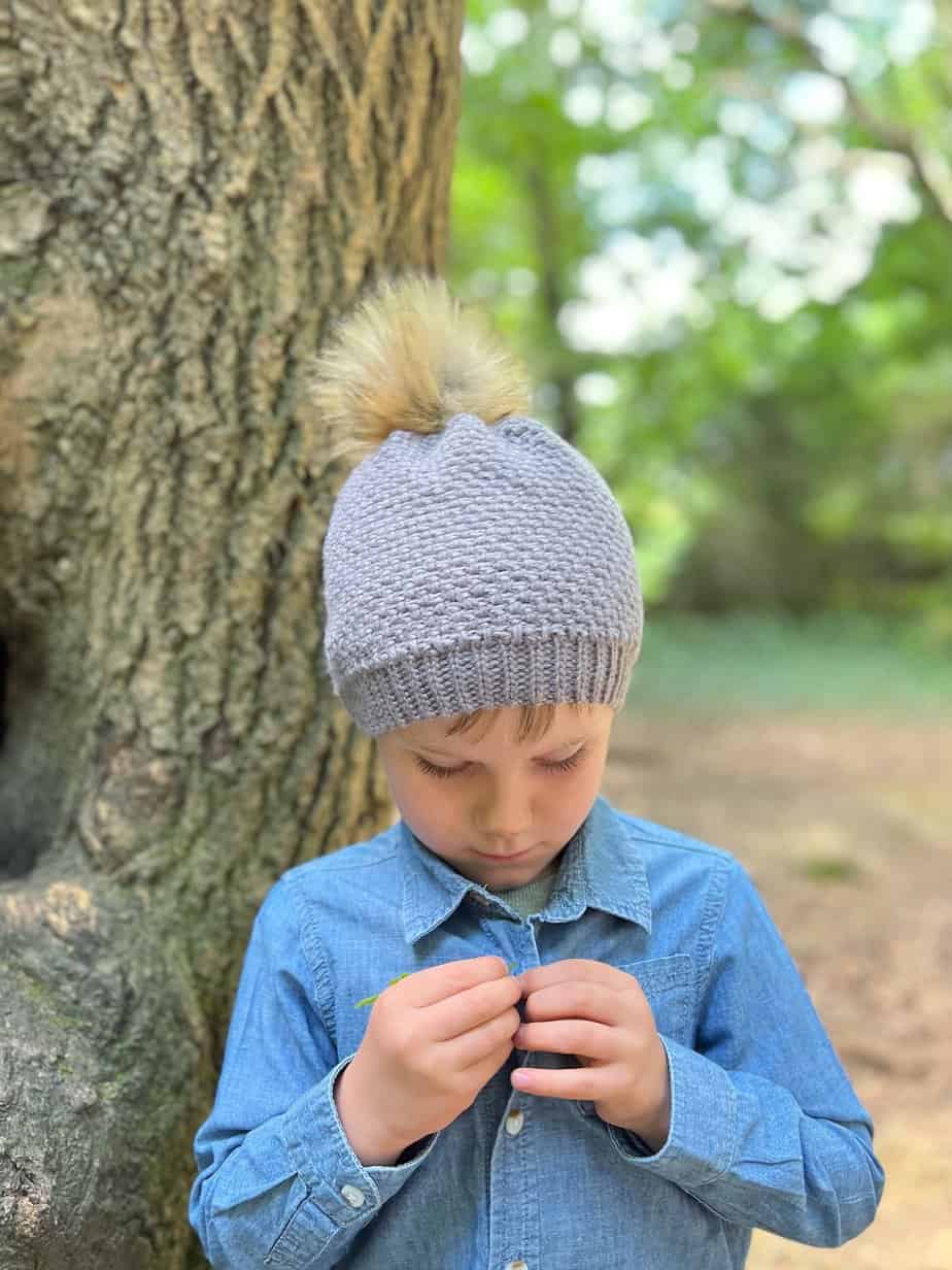 Young child wearing grey crochet hat with textured moss stitch pattern.