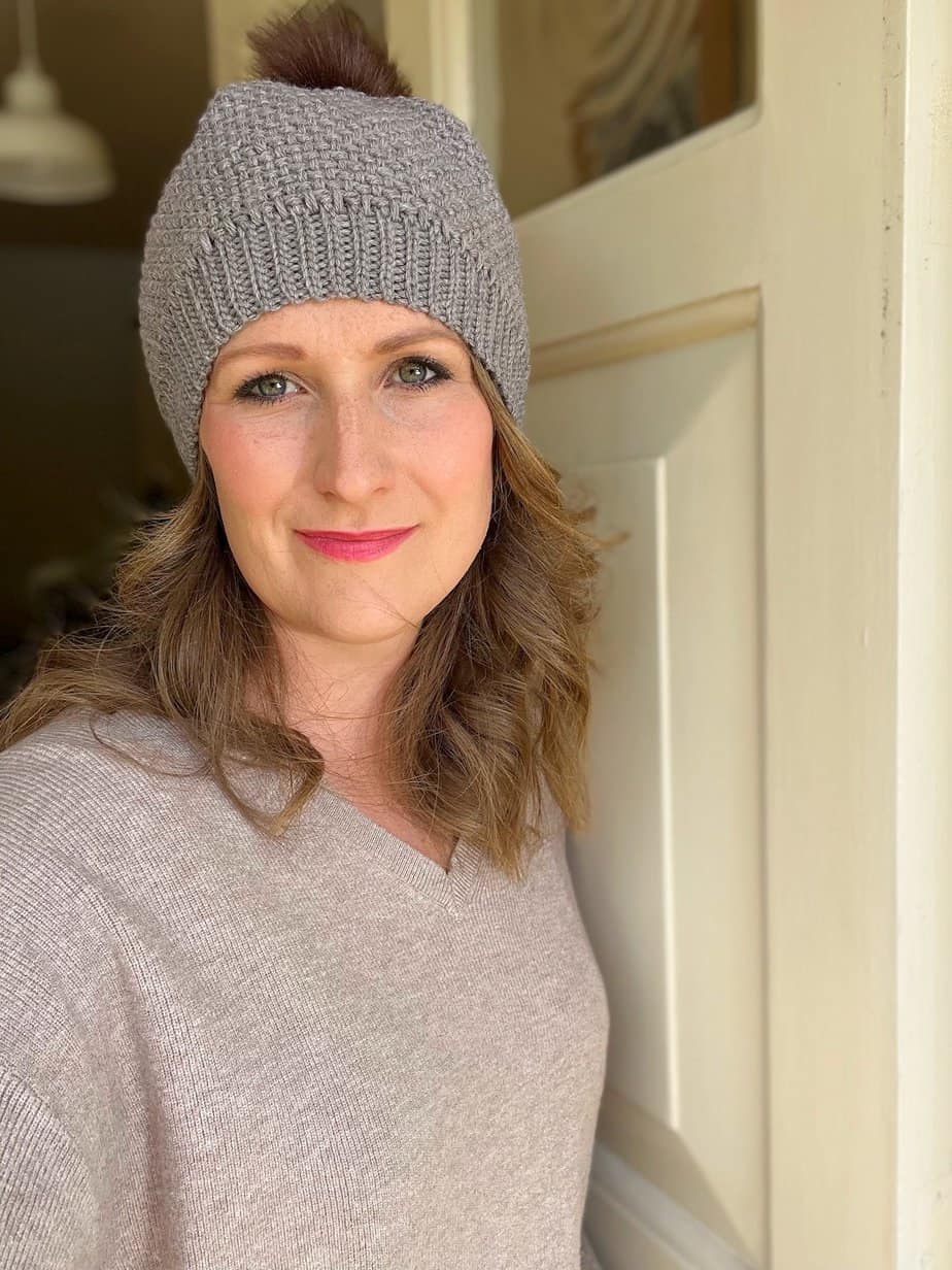 Woman standing in doorway wearing textured crochet with pom pom.