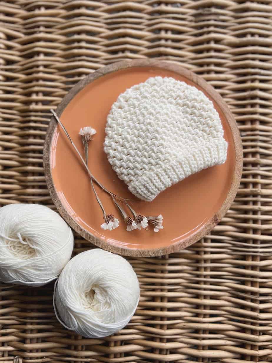 Cream newborn crochet hat pattern laid on wicker basket.