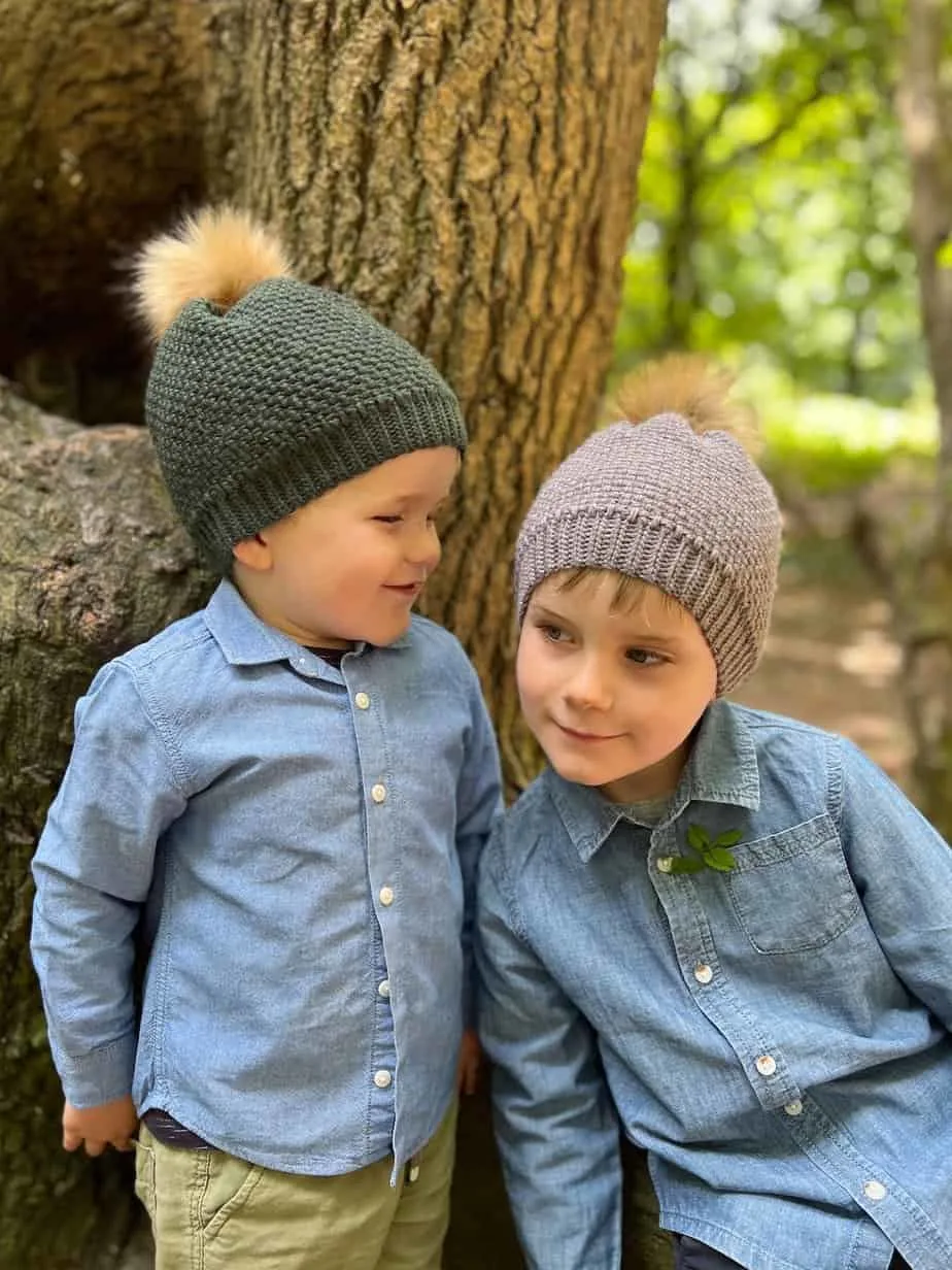 Two children wearing cosy crochet hats in the woods.