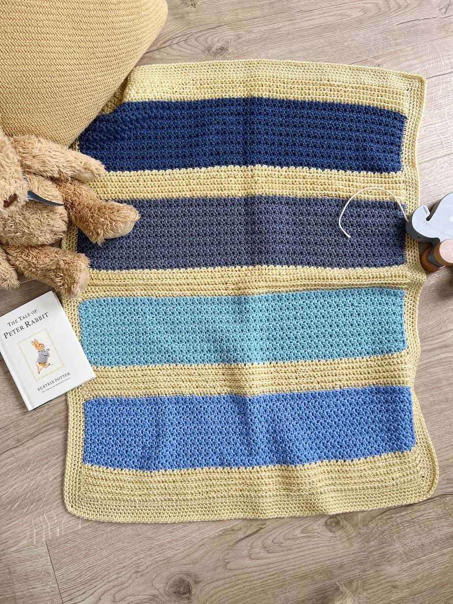 Modern crochet baby blanket pattern for boys with teddy, cushion and book.