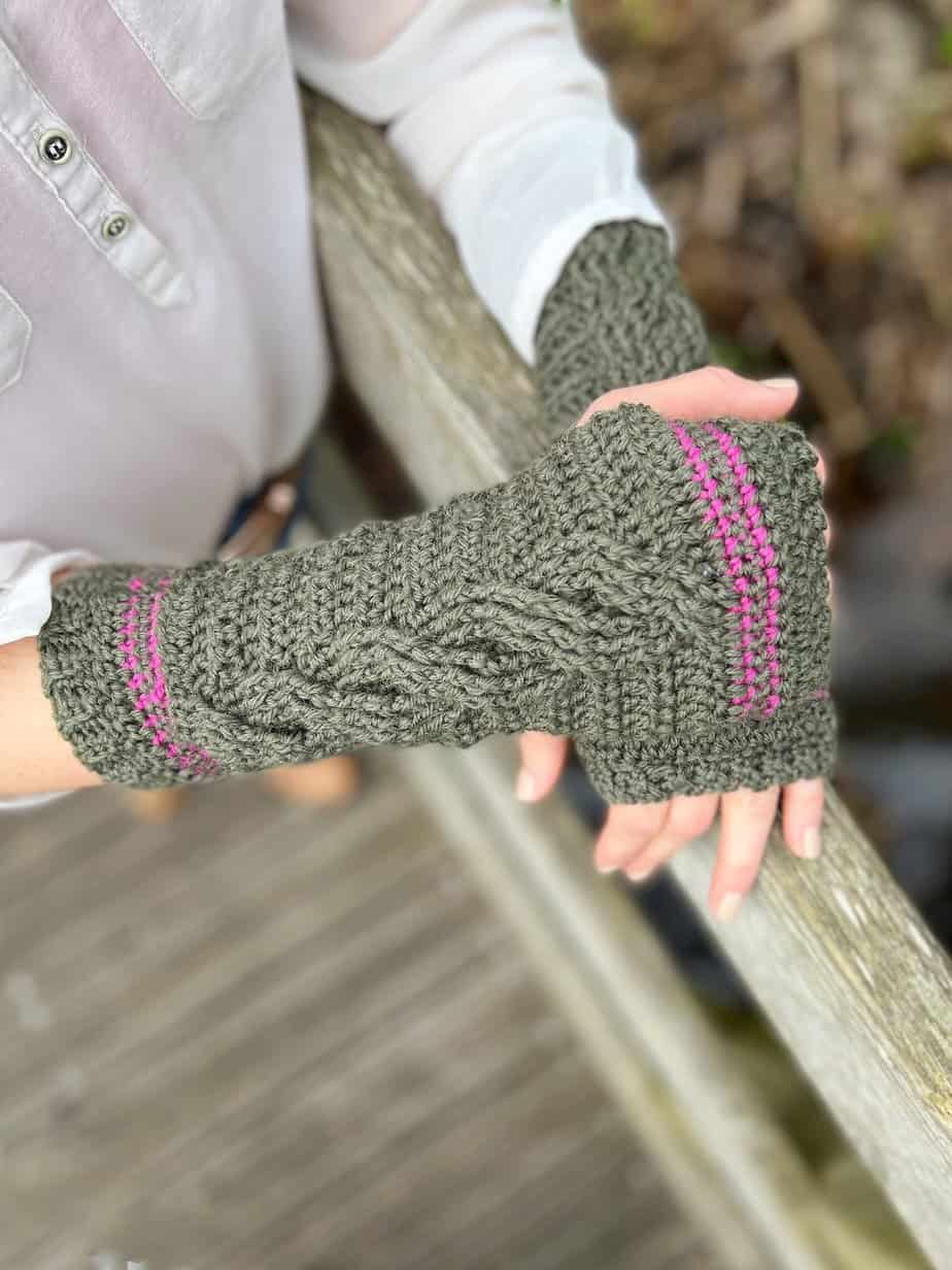 Woman leaning on bridge wearing green cable crochet wrist warmers.