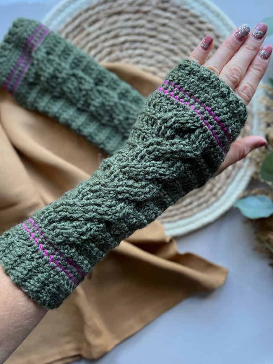 Crochet cable wrist warmer pattern on female hand with second mitten in background.