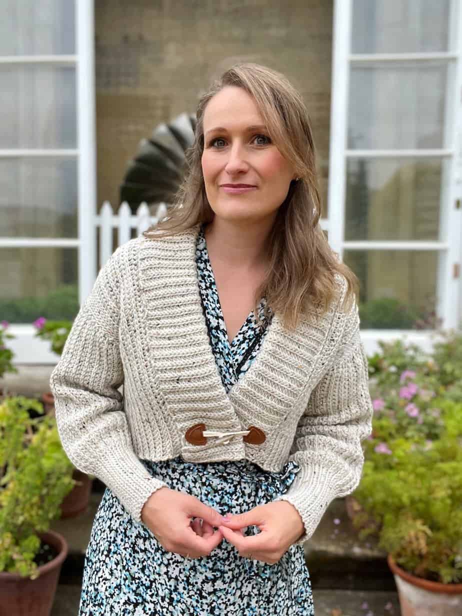 Woman wearing short crochet cardigan over a maxi dress in a garden.