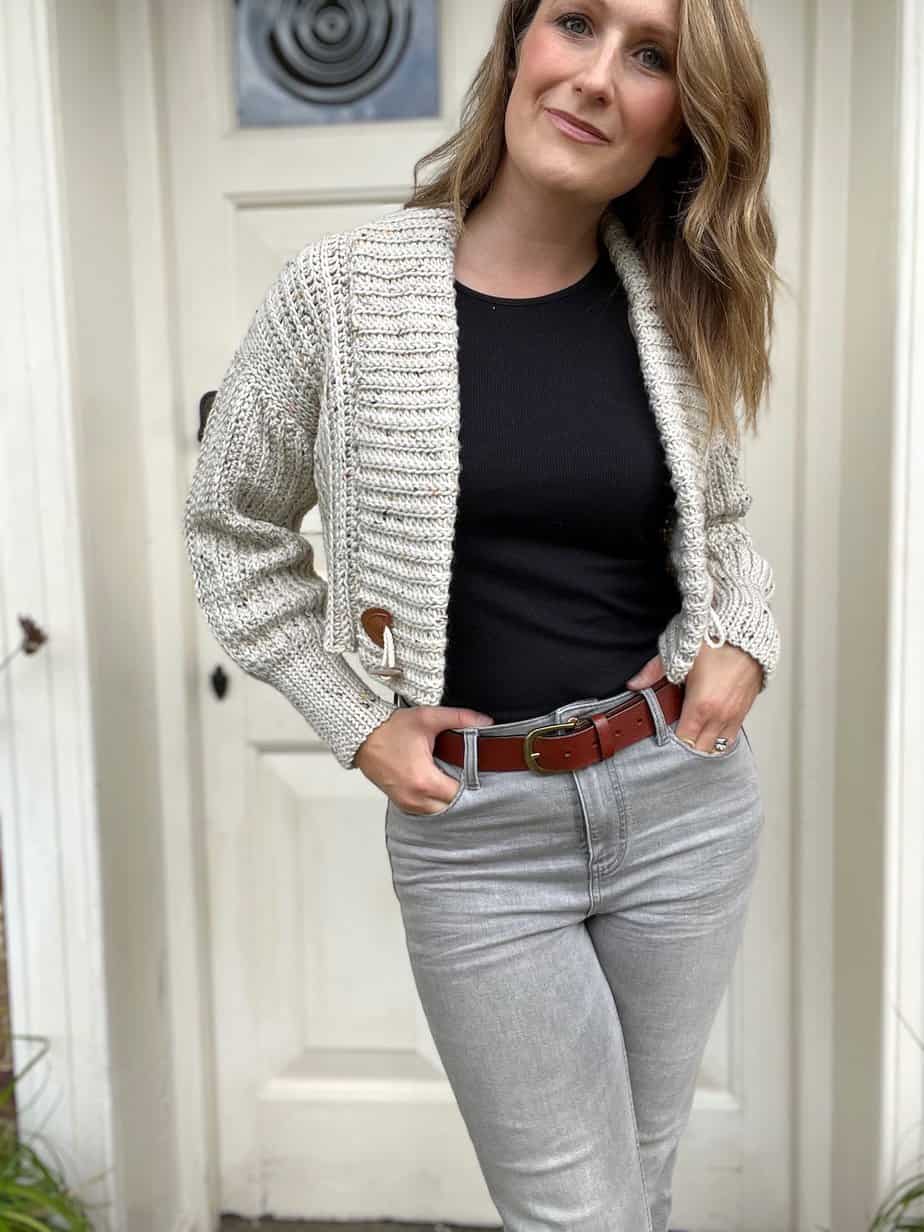 Woman wearing crop crochet cardigan pattern with hands in jeans pockets.