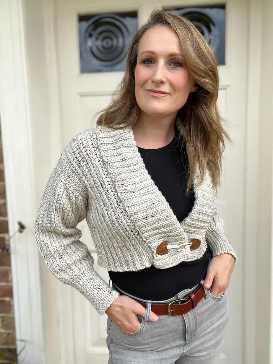 Woman wearing cropped crochet cardigan with toggle fastening.