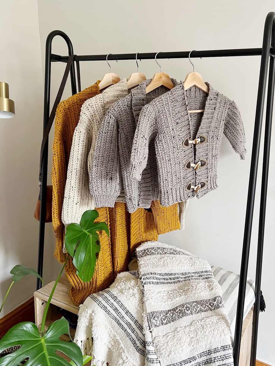 Four crochet cardigan patterns in adult and child sizes hanging on rail.