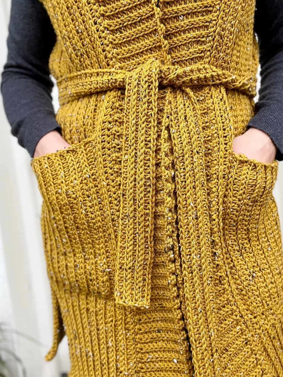 Person wearing crochet cardigan vest with hands in pockets.