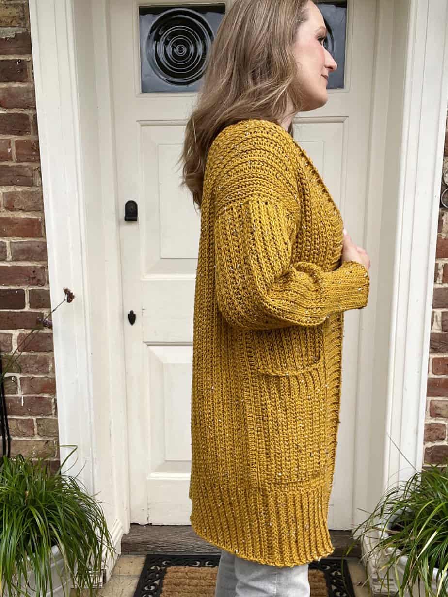 Woman standing sideways wearing long duster length crochet cardigan.