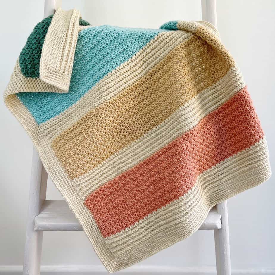 Striped baby blanket crochet pattern in bright colours on a ladder.