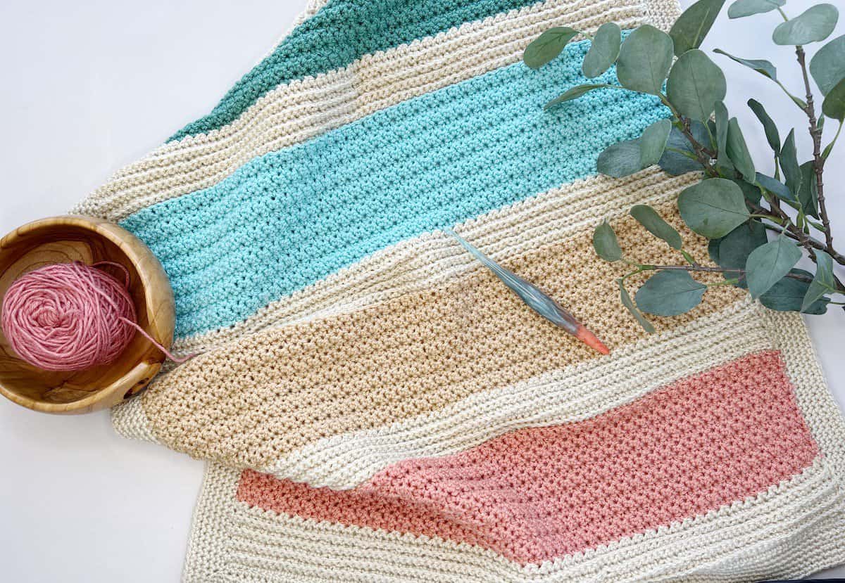 Easy striped crochet blanket pattern with yarn and hook.