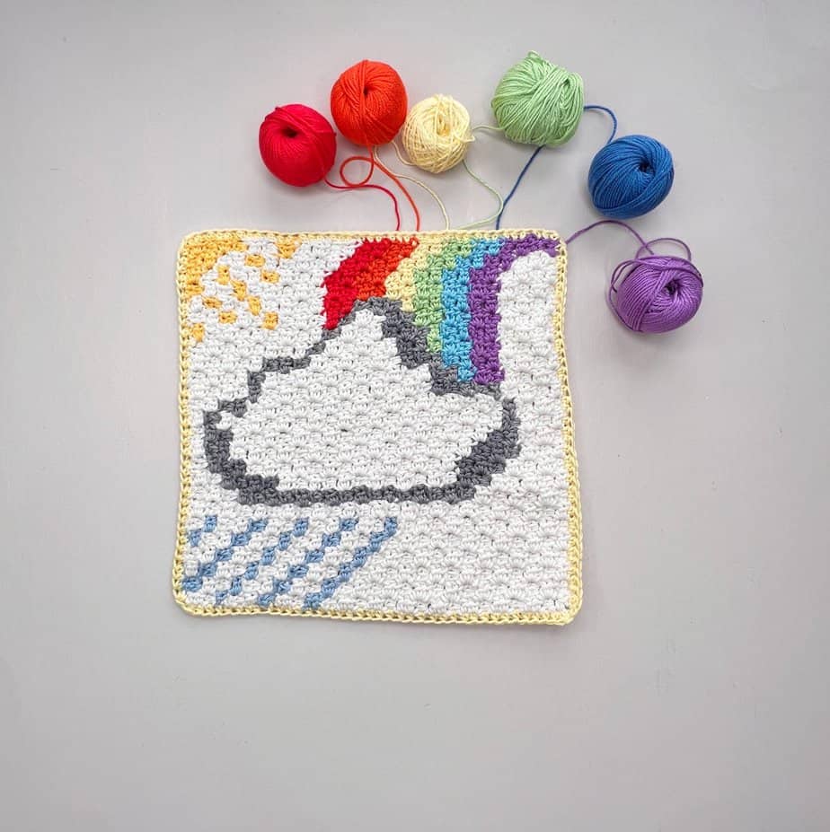 C2C crochet square with a cloud, rainbow and yarn laid around it.